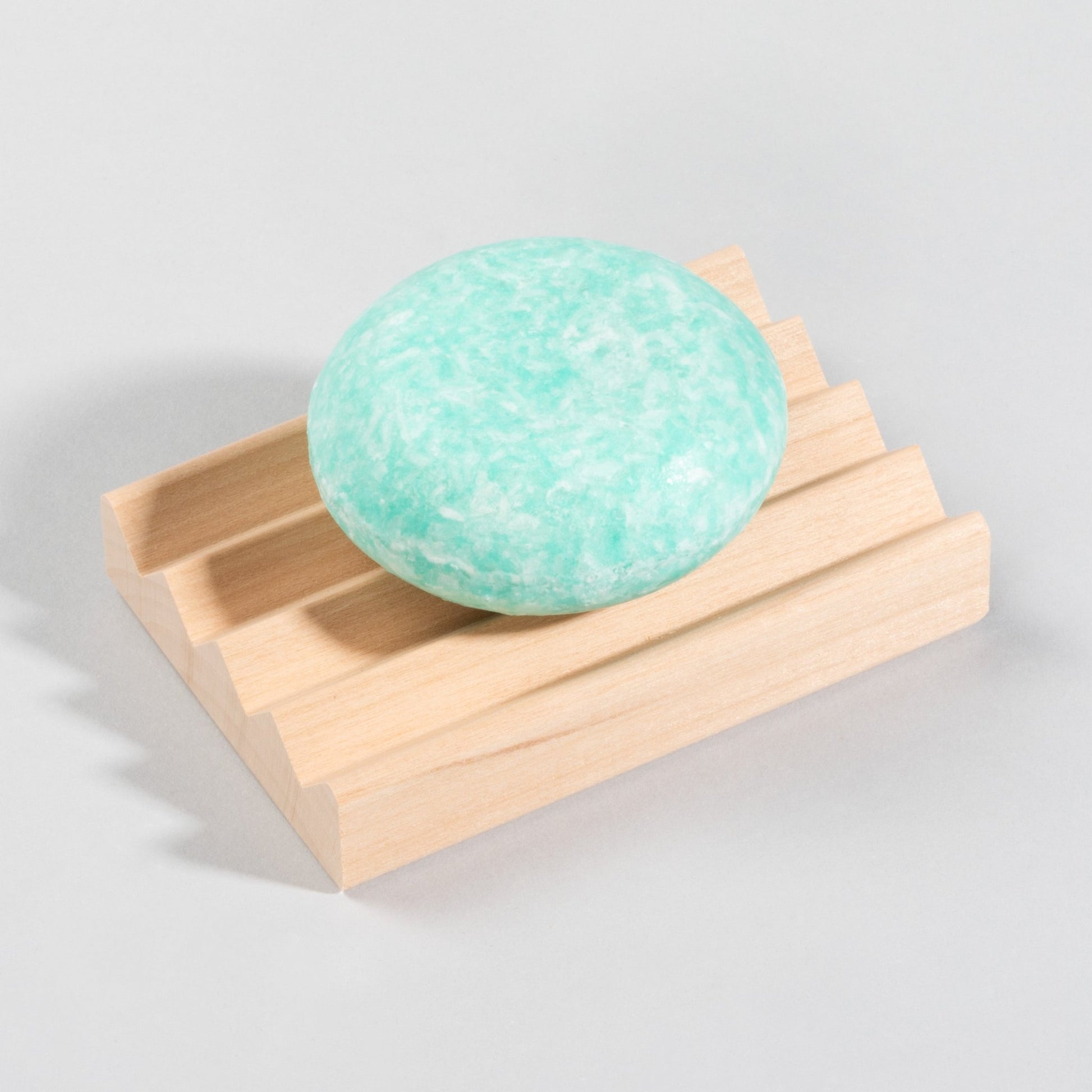 A peppermint ice natural shampoo bar on a solid wood soap dish. 