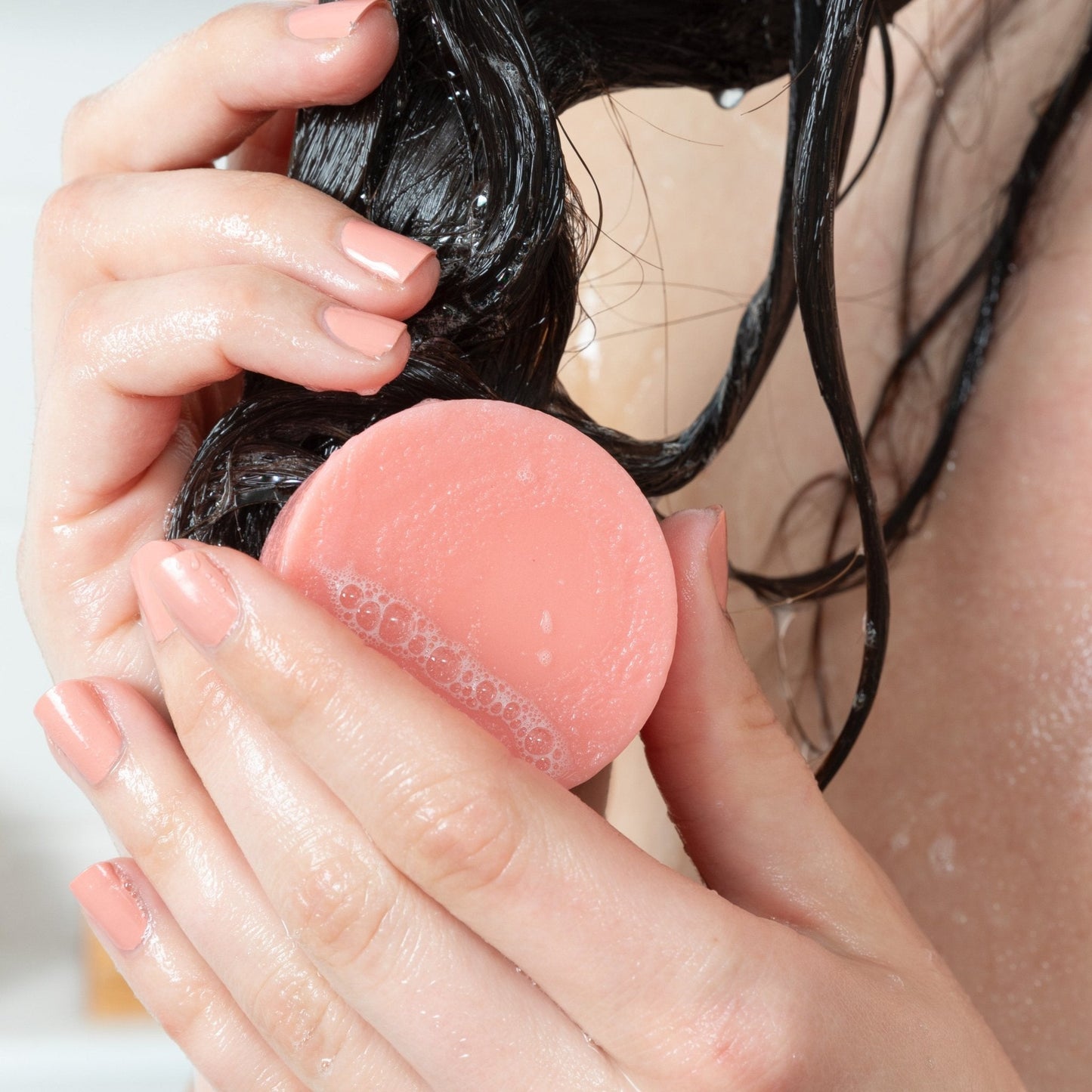 A woman with healthy, shiny hair uses a Citrus Squeeze natural conditioner bar by Community Goods.